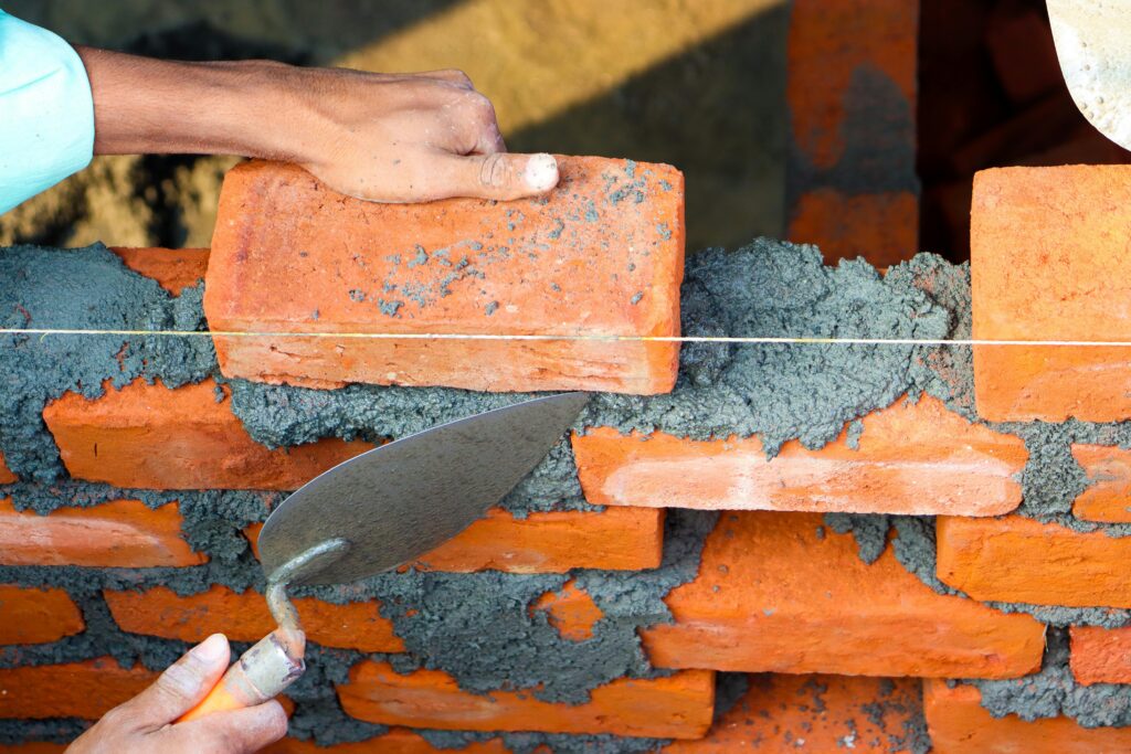 Hands laying bricks with cement in a construction setting, showcasing precise masonry work.